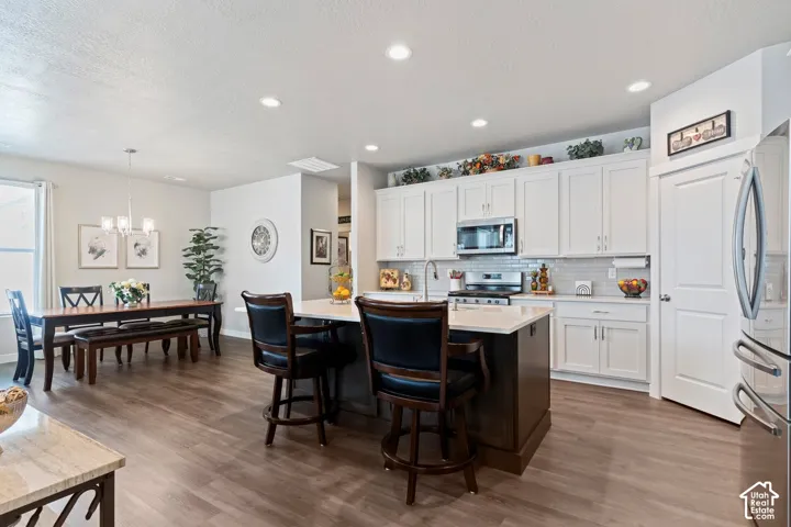 Kitchen with white cabinetry, stainless steel appliances, a center island with seating, and wood-finish flooring