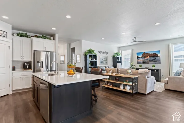 Kitchen island with white countertop and integrated sink, stainless steel appliances, wood-finish flooring, white cabinetry, and recessed lighting