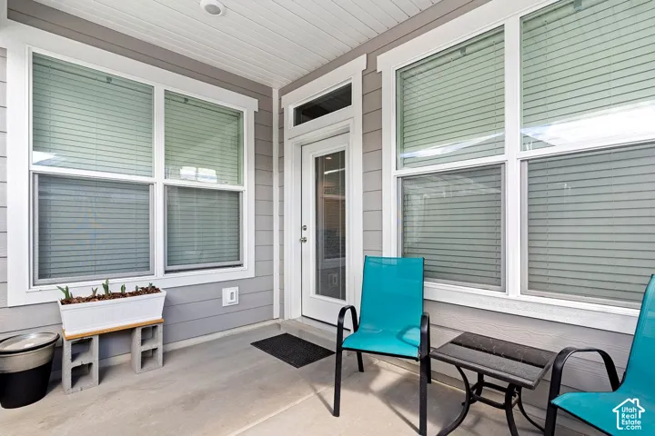 Covered concrete patio with siding exterior, multiple windows, and a glass-paneled door