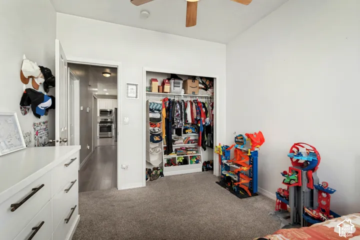 Carpeted room with a ceiling fan, a closet with built-in shelving, and a doorway opening to a hallway