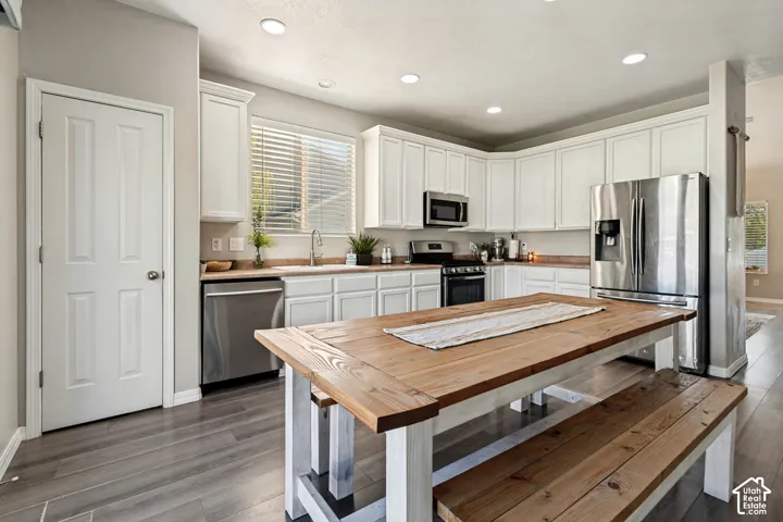 Kitchen featuring extensive white cabinetry, stainless steel appliances, recessed lighting, wood-finish flooring, and a large window