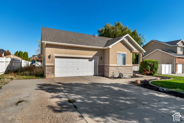 Attached two-car garage with a concrete driveway, stucco exterior with brick accents, and a landscaped front yard with a manicured lawn
