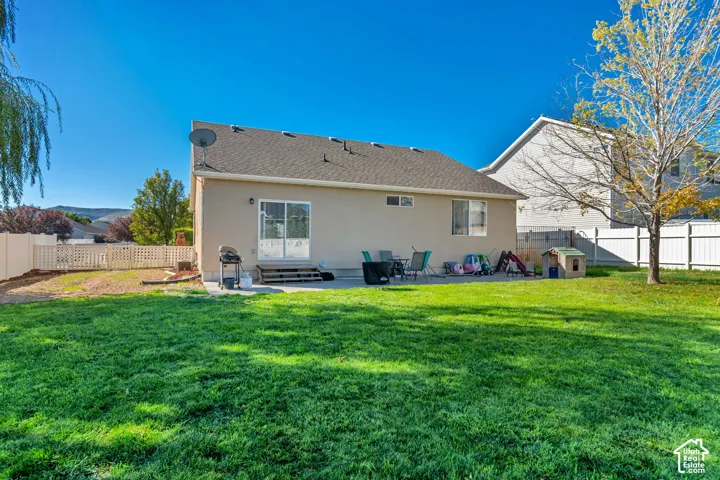 Expansive lawn area, concrete patio, sliding glass door access, white vinyl fencing, and a mature tree