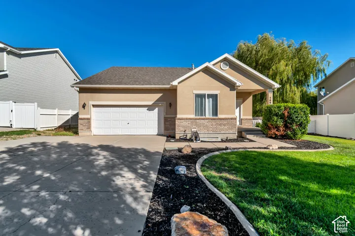 Stucco and brick facade with an attached garage, covered front entry, concrete driveway, and a landscaped front yard with a white picket fence