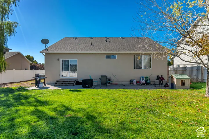 Expansive grassy yard with a concrete patio, sliding glass door, and a privacy fence