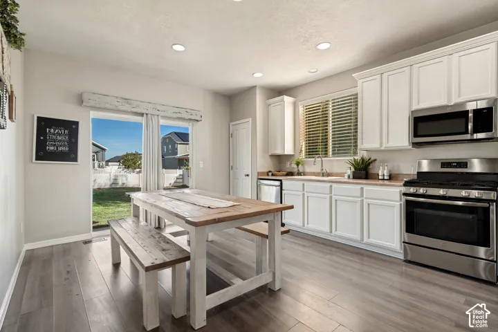 Kitchen with white cabinetry, wood-finish countertops, stainless steel appliances, and wood-finish flooring