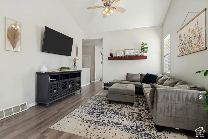 Vaulted ceilings, wood-finish flooring, ceiling fan with integrated lighting, wall-mounted display shelf, and built-in media console
