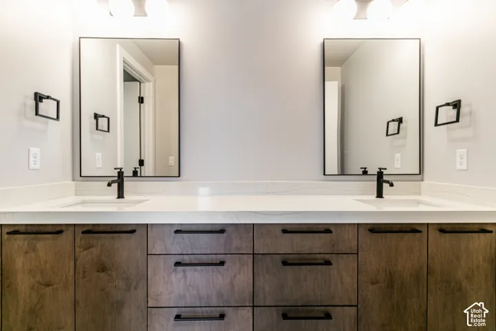 Dual vanity with light-tone countertop, wood-finish cabinetry, rectangular undermount sinks, and matte black fixtures