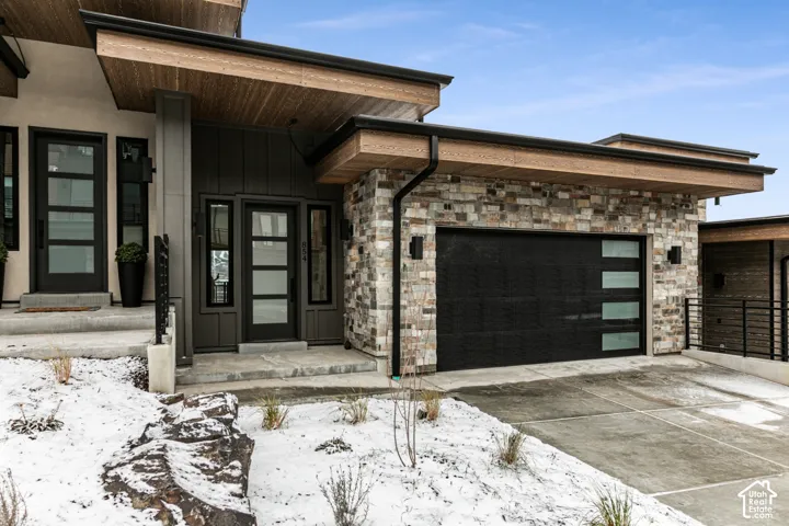 Contemporary exterior featuring stone accents, a modern garage door with frosted glass panels, wood-finish soffits, and black-framed entry doors