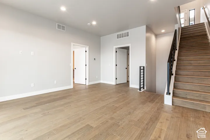 Wood-finish flooring throughout, recessed ceiling lighting, and a contemporary staircase with dark railing