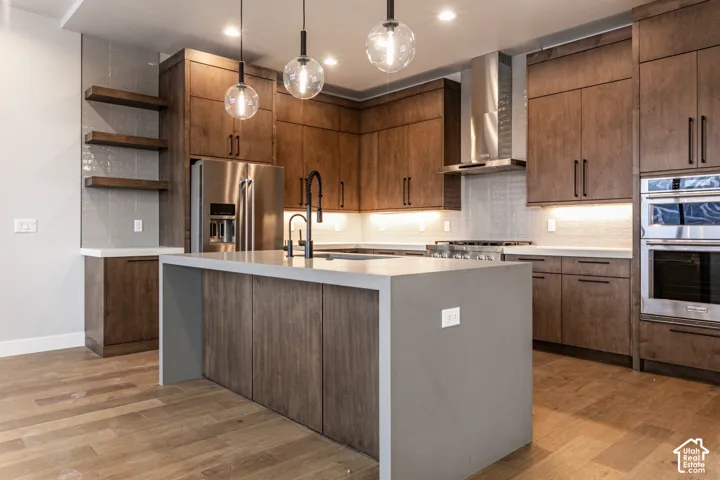 Kitchen featuring a central island, wood-finish flooring, stainless steel appliances, dark wood cabinetry, and pendant lighting