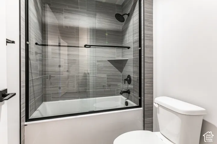 Bathtub and shower combination featuring a glass enclosure with matte black trim, gray tile surround, and a built-in shower niche