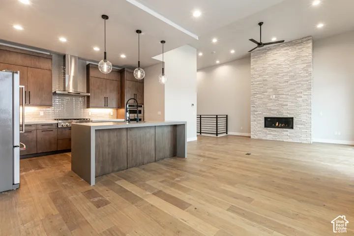 Open-concept kitchen and living area featuring wood-finish flooring, a contemporary fireplace with a stacked stone facade, a kitchen island with a waterfall edge, and stainless steel appliances