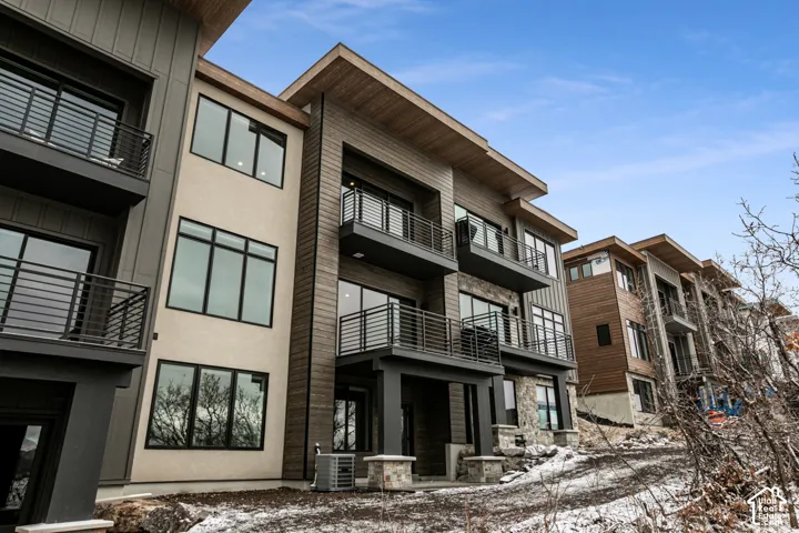 Multi-story exterior with horizontal wood-finish siding, stucco accents, stone detailing, black-framed windows, and multiple balconies with dark metal railings