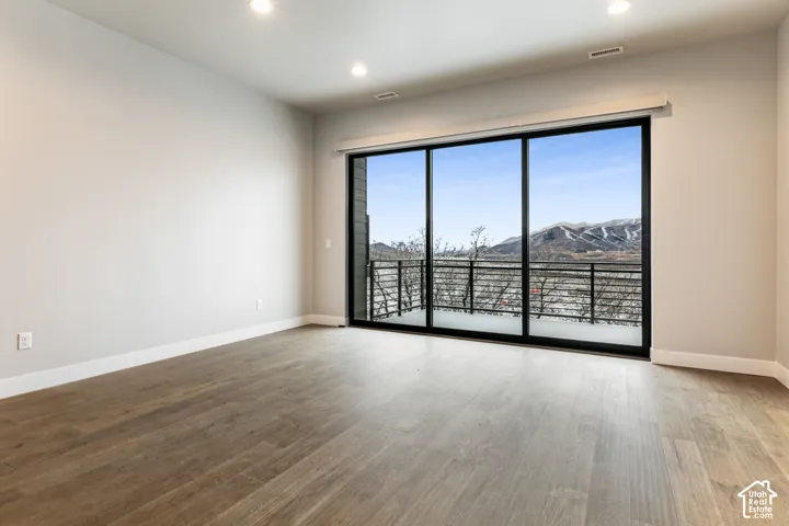 Spacious room featuring wood-finish flooring, recessed lighting, and a large sliding glass door opening to a balcony with black railings