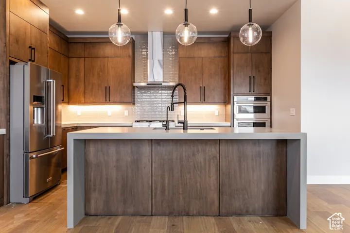 Kitchen featuring wood-finish cabinetry, stainless steel appliances, a center island with sink, and pendant lighting