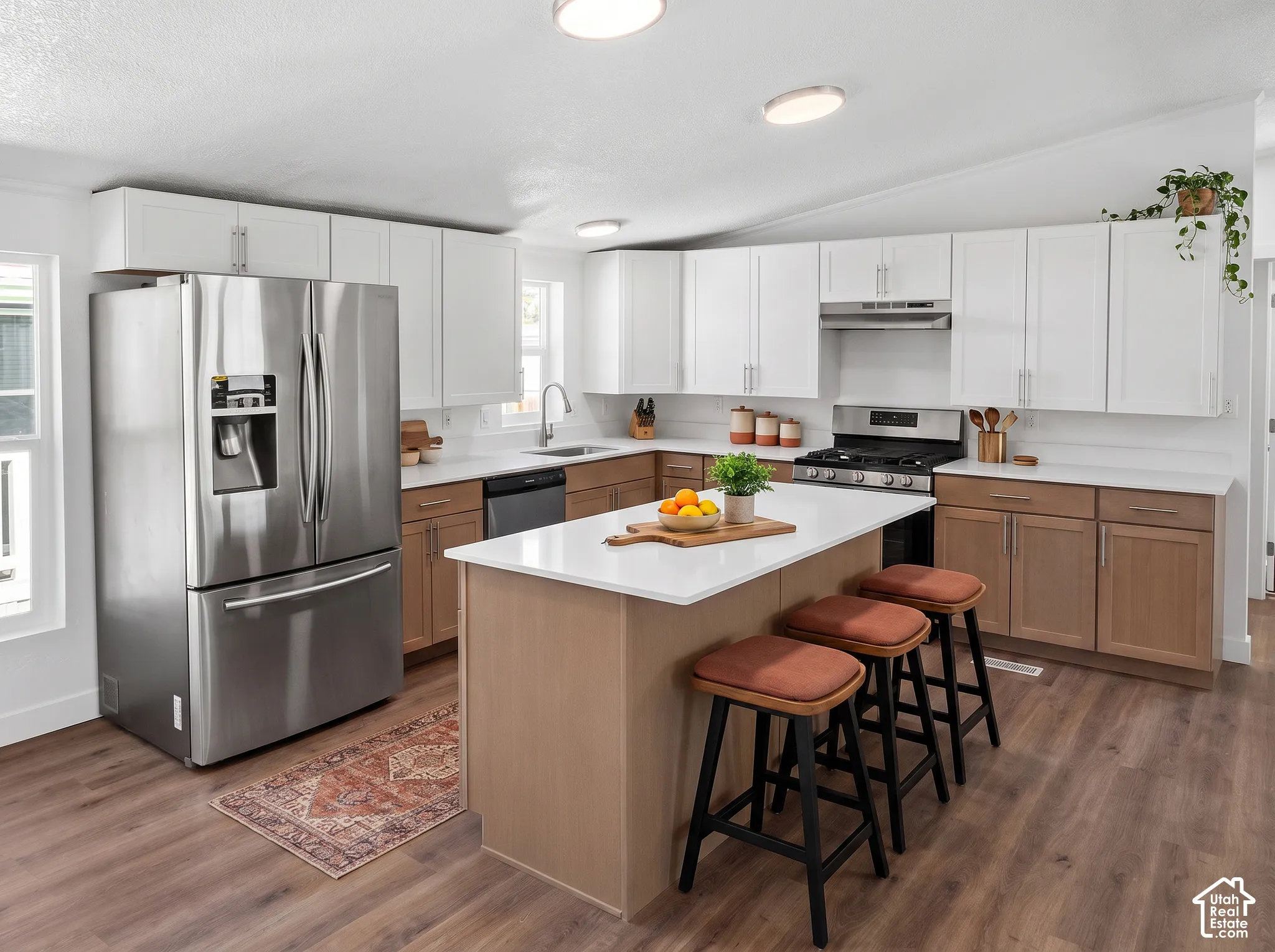 Kitchen featuring an integrated island with seating, a stainless steel appliance suite, white upper cabinetry, and wood-finish flooring