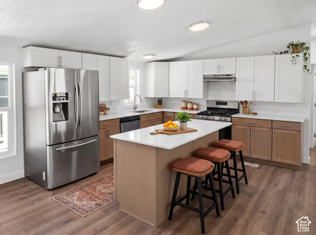 Kitchen featuring an integrated island with seating, a stainless steel appliance suite, white upper cabinetry, and wood-finish flooring