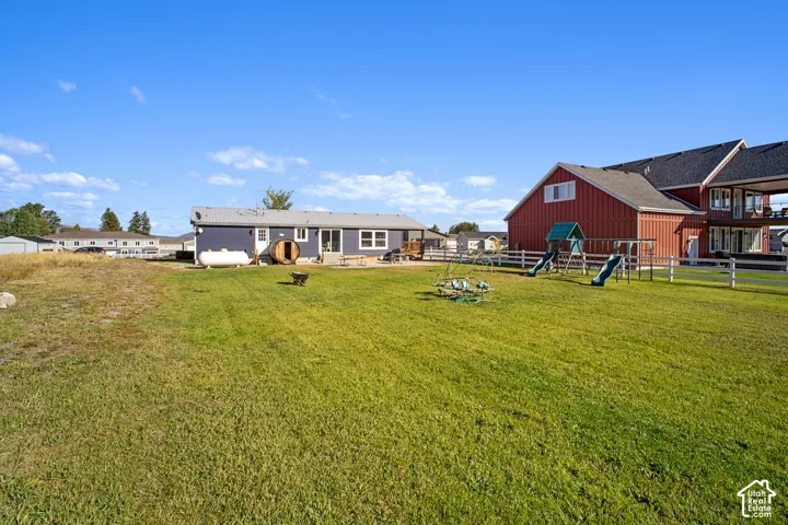 Expansive grassy yard with a white picket fence, a red barn-style structure, and a blue single-story residence