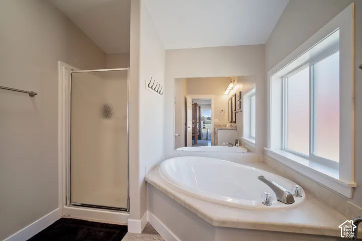 Spa-inspired primary bathroom showcasing a sunken soaking tub with integrated surround, large picture windows with natural light, separate walk-in shower with glass enclosure, dual vanity with stone countertop, and recessed ceiling lighting