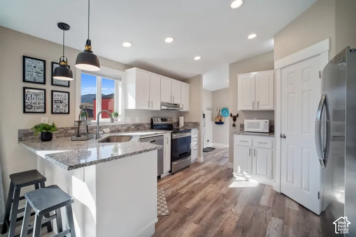 Kitchen featuring white cabinetry, stone-finish countertops, stainless steel appliances, and wood-finish flooring