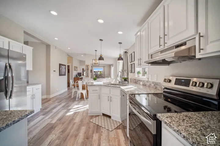 Kitchen featuring wood-finish flooring, white cabinetry, a kitchen island with pendant lighting, a stainless steel refrigerator, and a stainless steel oven range