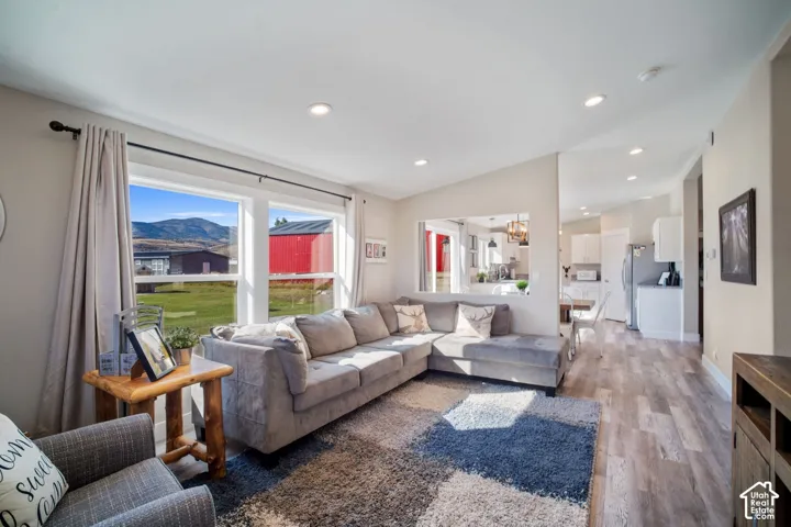 Expansive windows framing mountain scenery, wood-finish flooring, recessed lighting, and a partial wall opening to a kitchen space