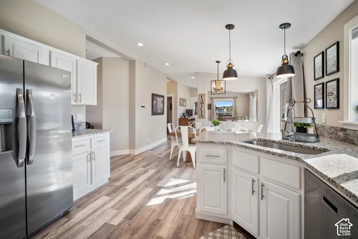 White cabinetry, stainless steel refrigerator, wood-finish flooring, granite countertops, and pendant lighting