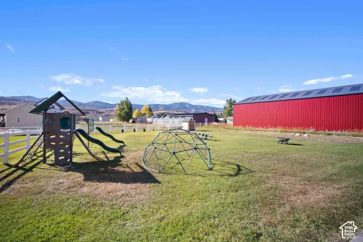 Expansive grassy area featuring a playset with slides, a geodesic dome, and a white fence