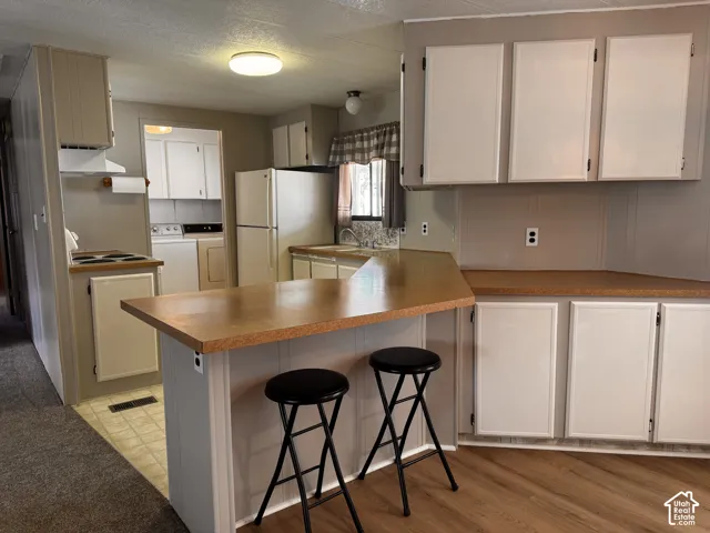 Kitchen featuring white cabinetry, light wood-finish countertops, wood-finish flooring, and an integrated breakfast bar