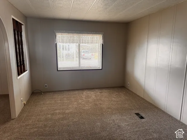 Neutral-toned carpeting with light gray wall paneling, a large window with horizontal blinds, and a decorative interior architectural opening