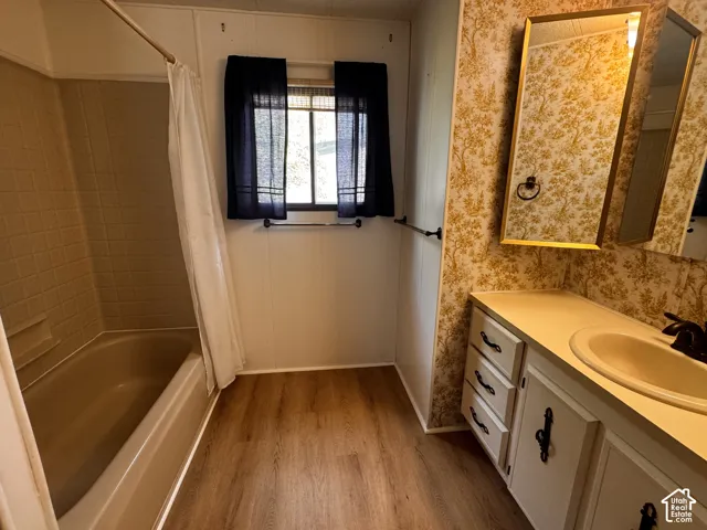 Bathroom featuring a built-in tub with tiled surround, wood-finish flooring, a vanity with integrated sink, and an overhead mirror