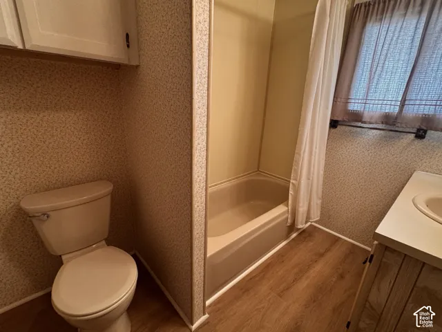 Built-in tub-shower combination, wood-finish flooring, vanity with integrated sink, and overhead cabinetry