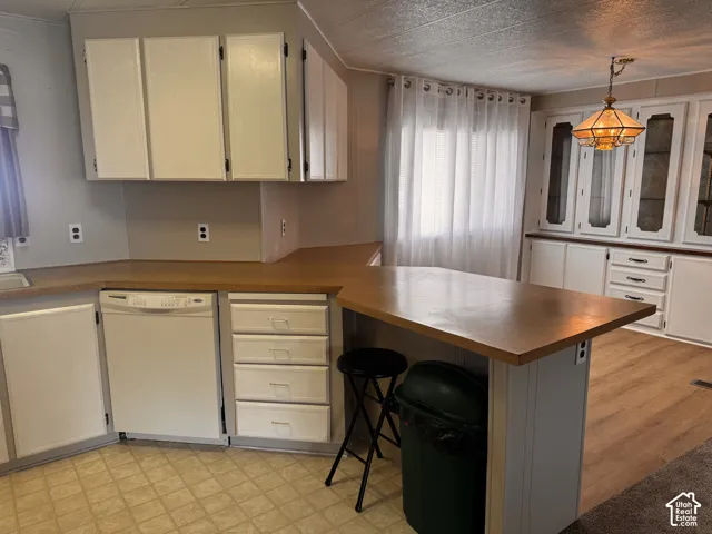 Kitchen featuring white cabinetry, light wood-finish countertops, a built-in dishwasher, and a breakfast bar