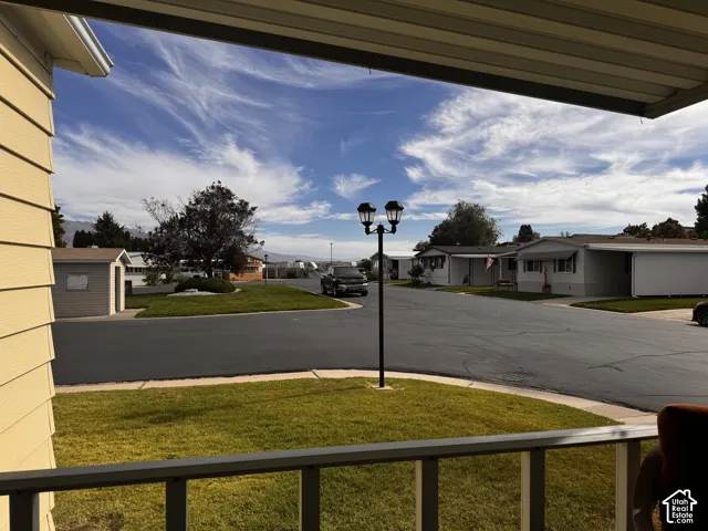 Outdoor porch with railing, manicured lawn, street light, paved road, and distant structures