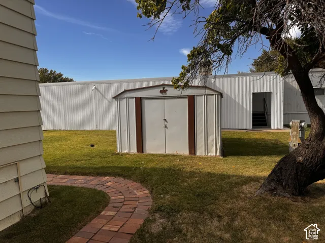 Metal storage shed with a peaked roof, brick pathway, and a large tree