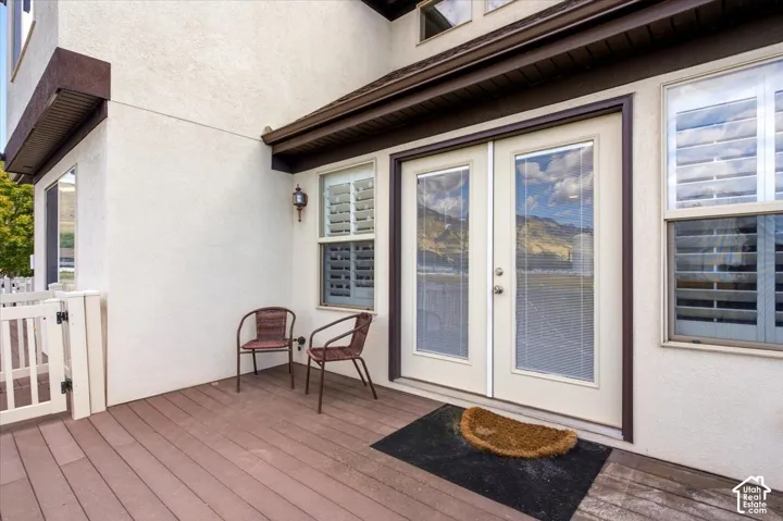 Private deck with composite wood-finish flooring, featuring a white picket gate, stucco exterior, and double glass-paned doors