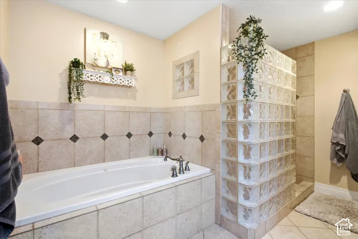 Tiled soaking tub with deck-mounted faucet, adjacent walk-in shower with glass block enclosure, and tiled walls with decorative accents