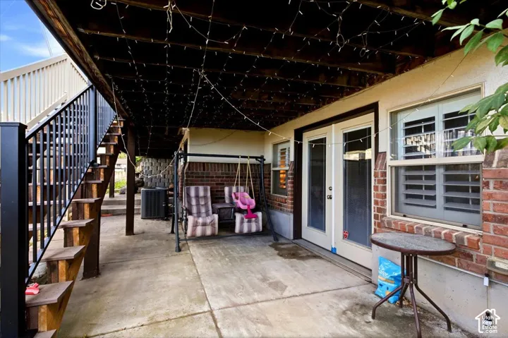 Patio featuring exposed brick, concrete flooring, exterior double doors, and a wood staircase with metal railings