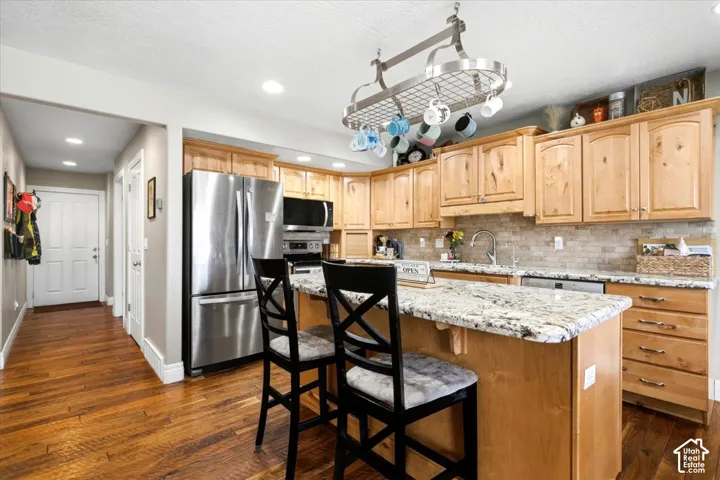 Kitchen featuring a stone-look tile backsplash, light wood-finish cabinetry, stainless steel appliances, and a central island with a light-colored countertop