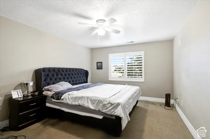 Carpeted flooring, ceiling fan with integrated lighting, and a window featuring plantation shutters