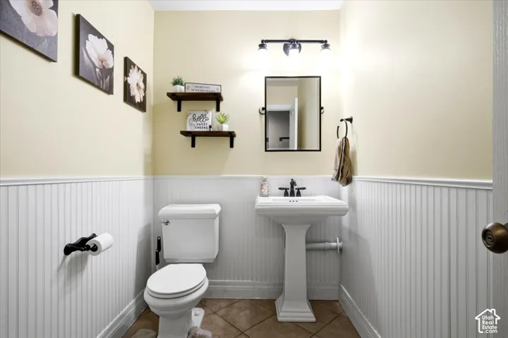 White beadboard wainscoting, pedestal sink with black hardware, wall-mounted mirror, and tile flooring