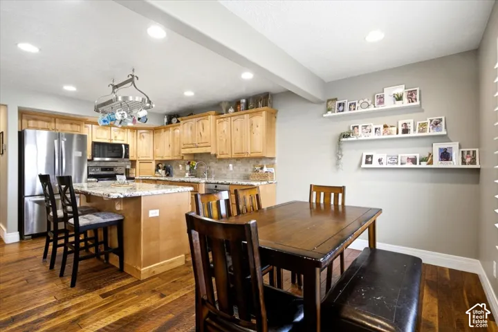 Wood-finish flooring throughout, featuring light wood cabinetry with stainless steel appliances, a kitchen island with stone countertops, and recessed lighting
