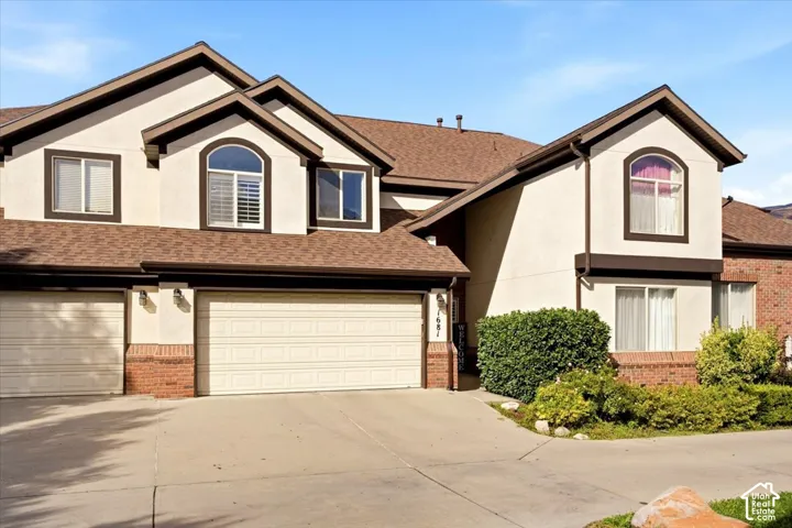 Stucco exterior with brick accents, multi-pane windows, arched window dormers, and an attached two-car garage