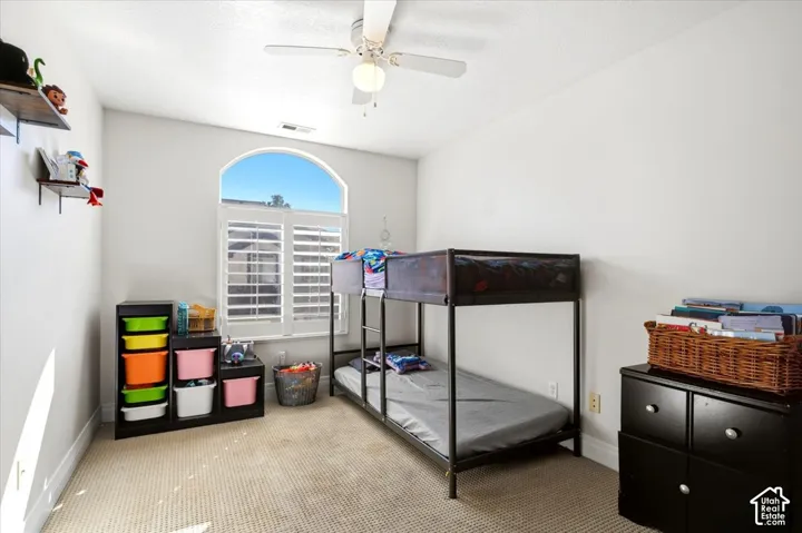 Arched window featuring white plantation shutters, textured carpeting, and a ceiling fan with integrated lighting