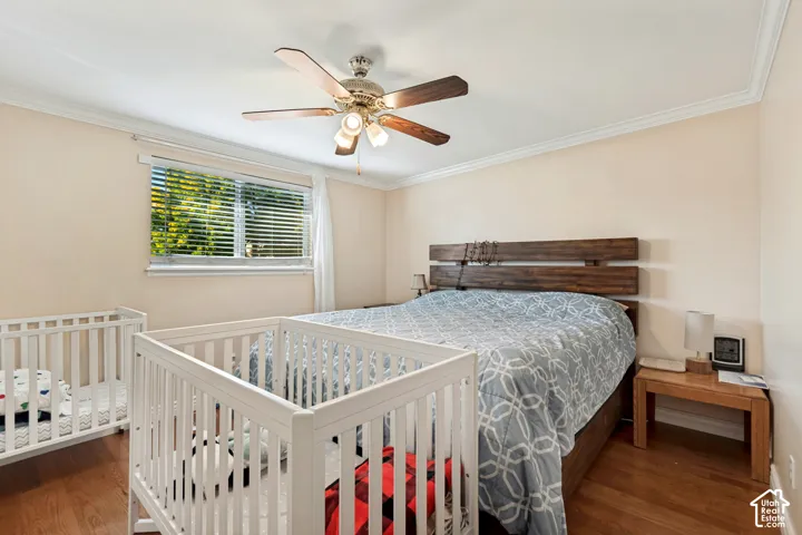 Crown molding detail, wood-finish flooring, ceiling fan with integrated lighting, window with blinds, wood headboard