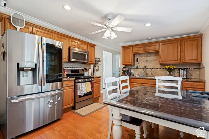 Kitchen featuring stainless steel appliances, wood cabinetry, granite-style countertops, tile backsplash, and wood-finish flooring