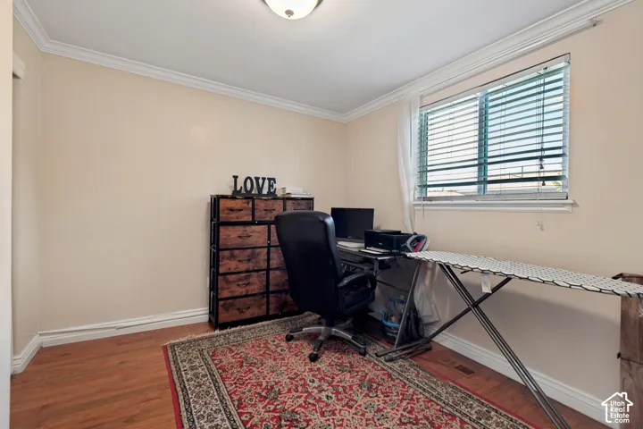 Wood-finish flooring, neutral wall tones, crown molding, and a bright window with blinds