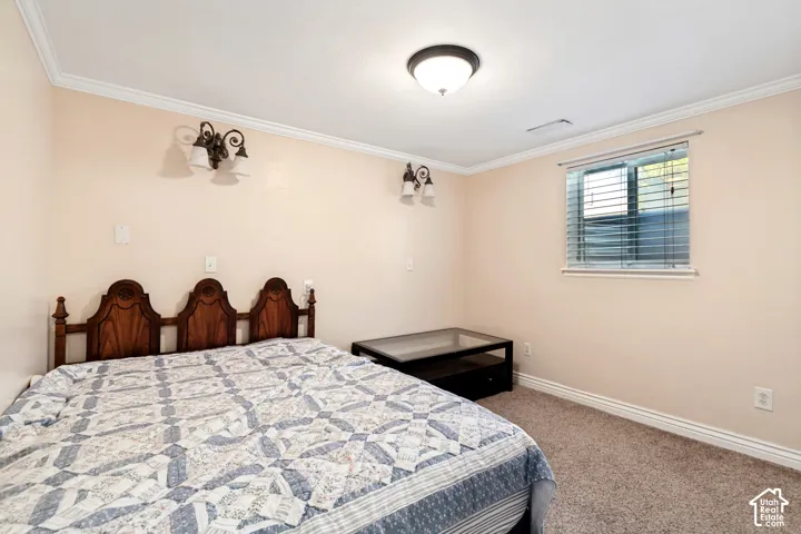 Wood-finish headboard, built-in wall sconces, ceiling-mounted light fixture, crown molding, and a window with blinds