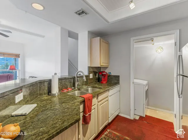 Kitchen featuring granite countertops, a double basin stainless steel sink with a gooseneck faucet, light wood-finish cabinetry, and an integrated dishwasher